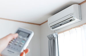 Hand holding remote pointing at ductless AC unit